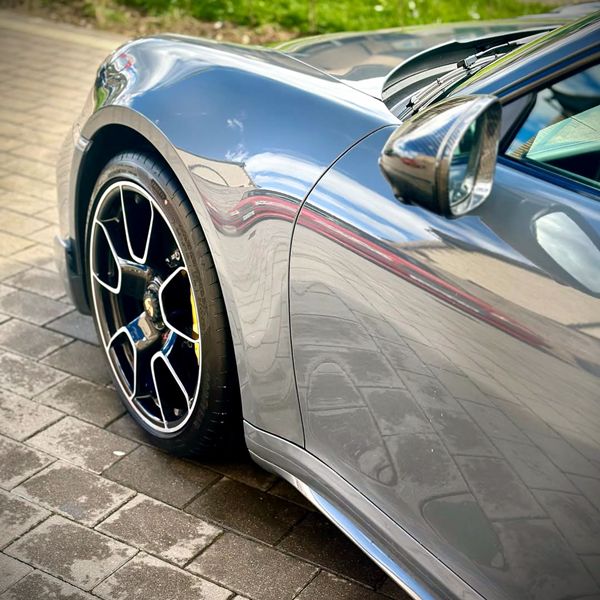Front left wing and alloy wheel of a cobalt Porsche viewed from an angle behind, highlighting ceramic protection.