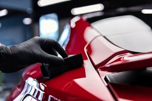 Professional car detailer applying a protective ceramic coating layer to the car exterior surface.