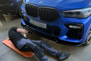 In our professional auto detailing workshop in Mullingar, a technician aligns and fits a front lip from the complete body kit of a blue luxury vehicle.