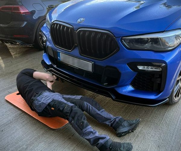 In our professional auto detailing workshop in Mullingar, a technician aligns and fits a front lip from the complete body kit of a blue luxury vehicle.